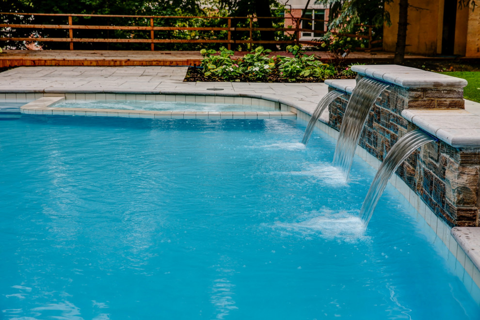 Пример оригинального дизайна: большой прямоугольный бассейн на заднем дворе в стиле неоклассика (современная классика) с джакузи и покрытием из каменной брусчатки