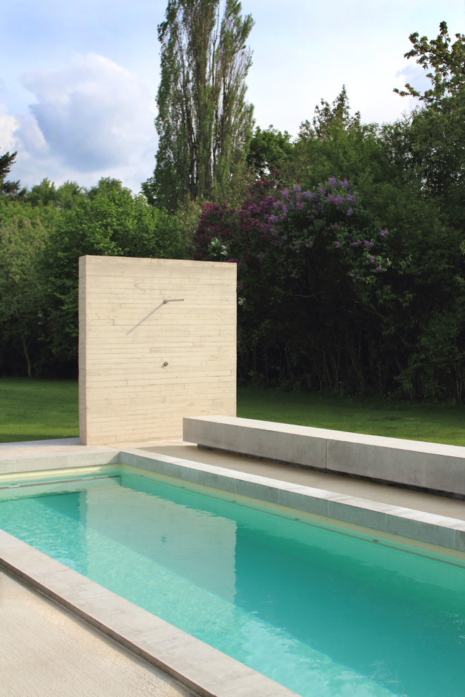 Modelo de piscina con tobogán alargada minimalista grande rectangular en patio trasero con adoquines de hormigón