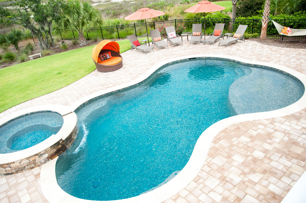 Foto di una grande piscina monocorsia tropicale a "C" dietro casa con una vasca idromassaggio e pavimentazioni in pietra naturale