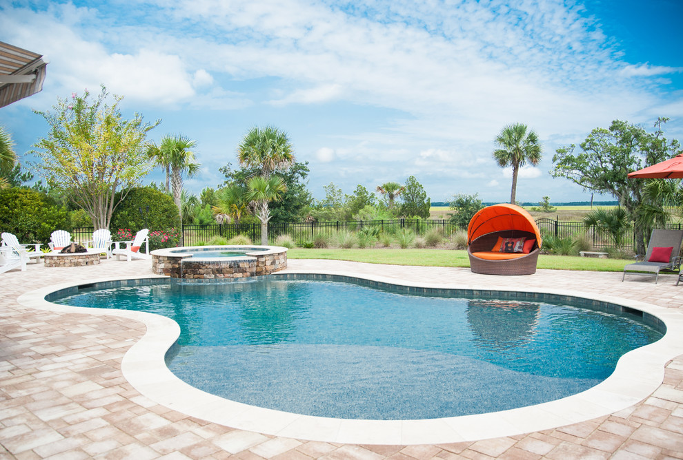 Idee per una grande piscina monocorsia tropicale a "C" dietro casa con una vasca idromassaggio e pavimentazioni in pietra naturale