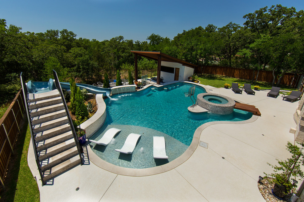 Modelo de piscina con tobogán natural clásica renovada grande a medida en patio trasero con losas de hormigón