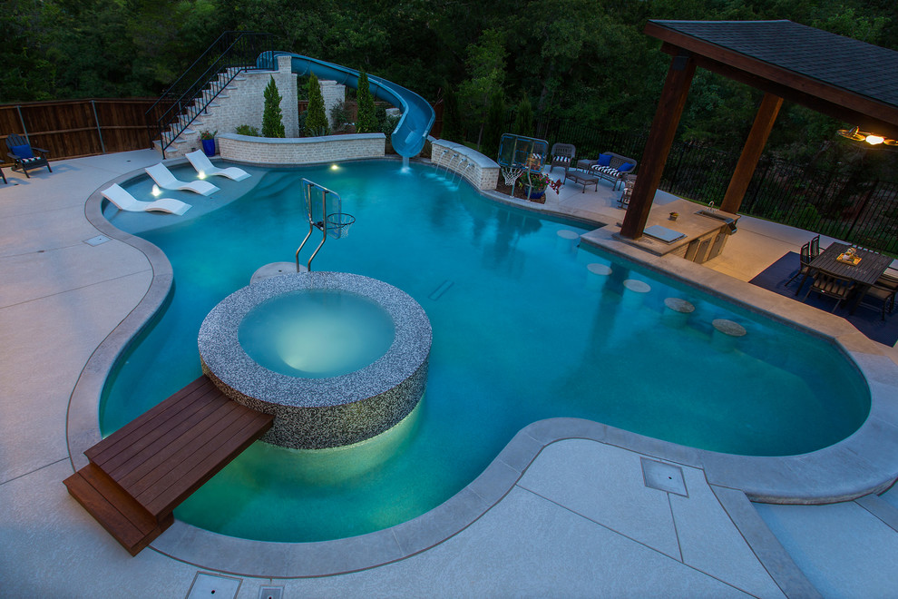 Immagine di una grande piscina naturale classica personalizzata dietro casa con un acquascivolo e lastre di cemento