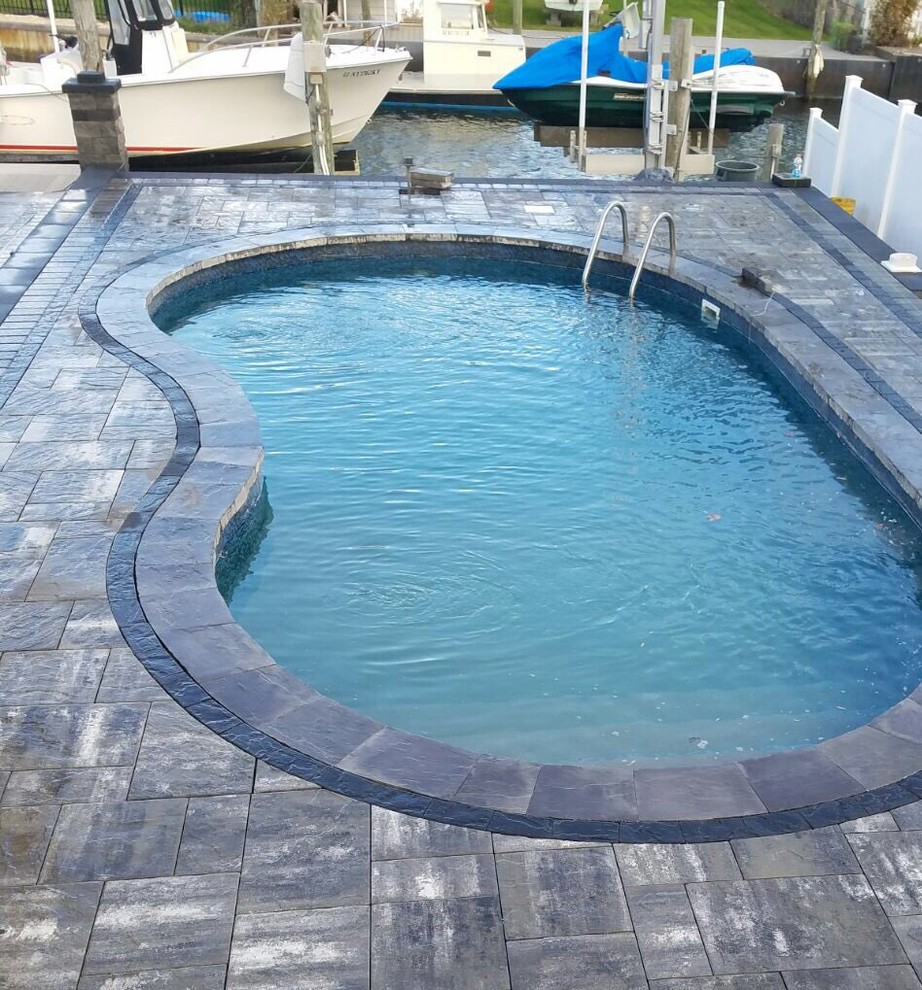 Large mediterranean back kidney-shaped natural swimming pool in New York with concrete paving.
