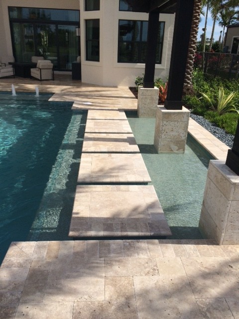 Ejemplo de piscina actual grande a medida en patio trasero con adoquines de piedra natural