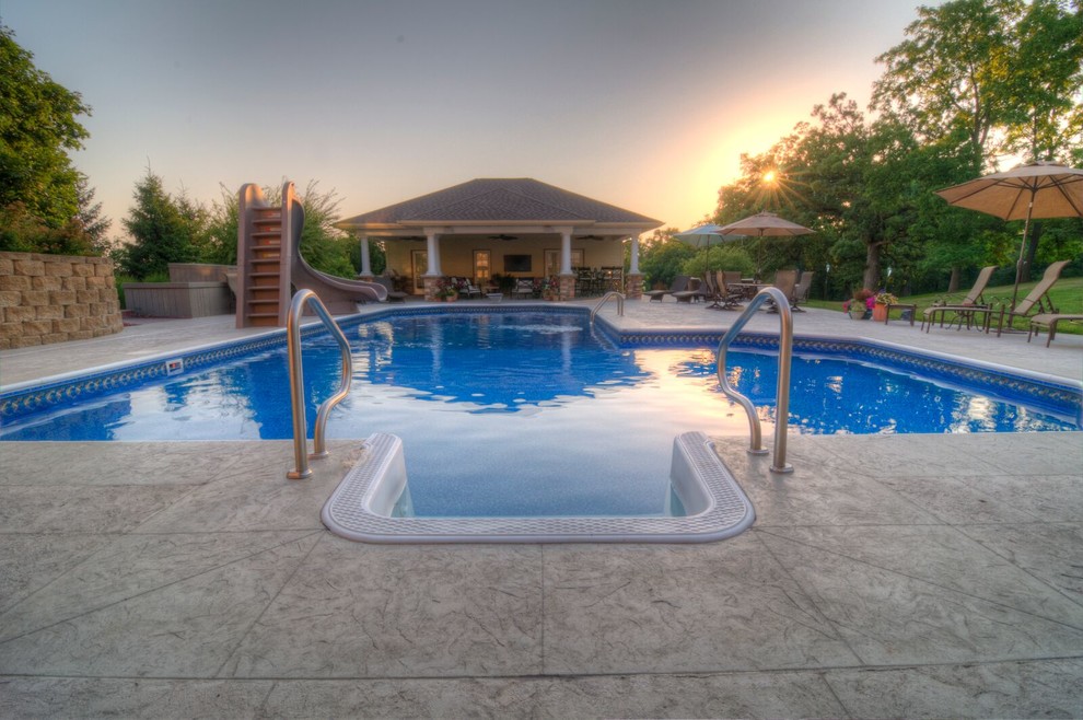 Modelo de piscina con tobogán natural tradicional renovada grande a medida en patio trasero con suelo de hormigón estampado