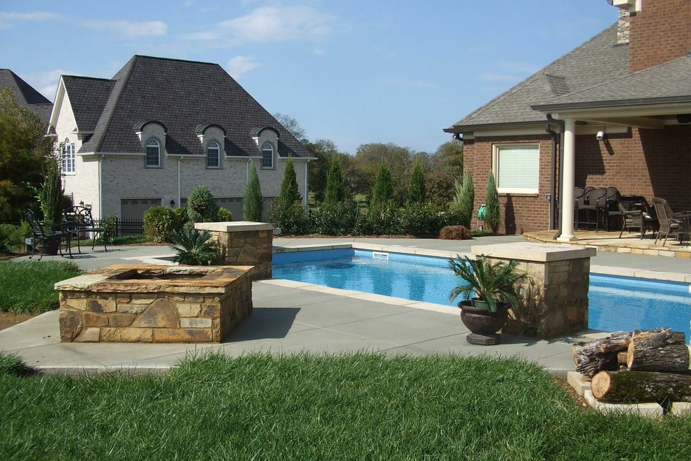 Modelo de piscina infinita actual grande rectangular en patio trasero con adoquines de hormigón