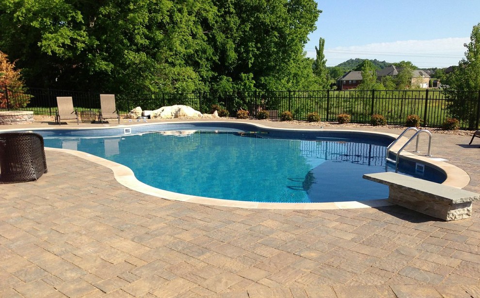 Imagen de piscina natural clásica de tamaño medio a medida en patio trasero con adoquines de hormigón