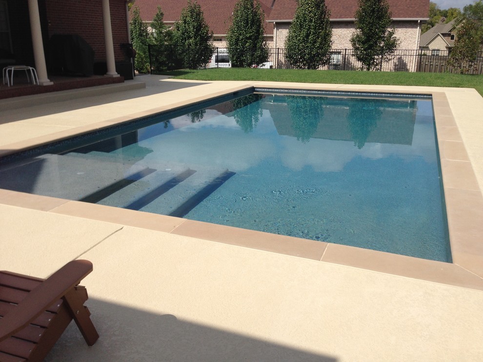 Ejemplo de piscina natural clásica de tamaño medio rectangular en patio trasero con losas de hormigón