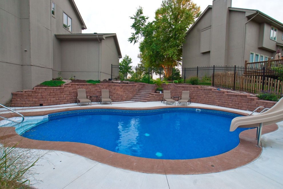 Foto di una grande piscina chic a "C" dietro casa con pavimentazioni in cemento e un acquascivolo