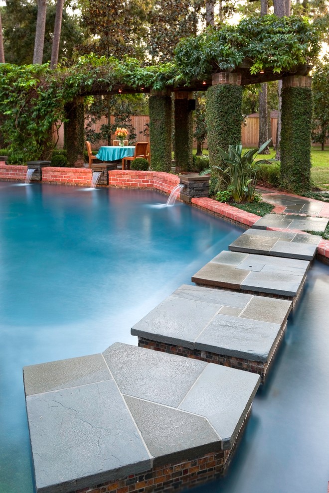 Inspiration for a large eclectic back custom shaped lengths swimming pool in Houston with a water feature and natural stone paving.