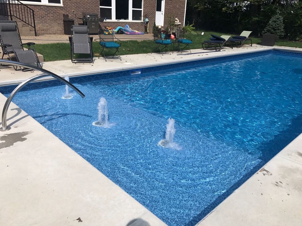 Modelo de piscina con fuente alargada minimalista de tamaño medio rectangular en patio trasero con suelo de hormigón estampado
