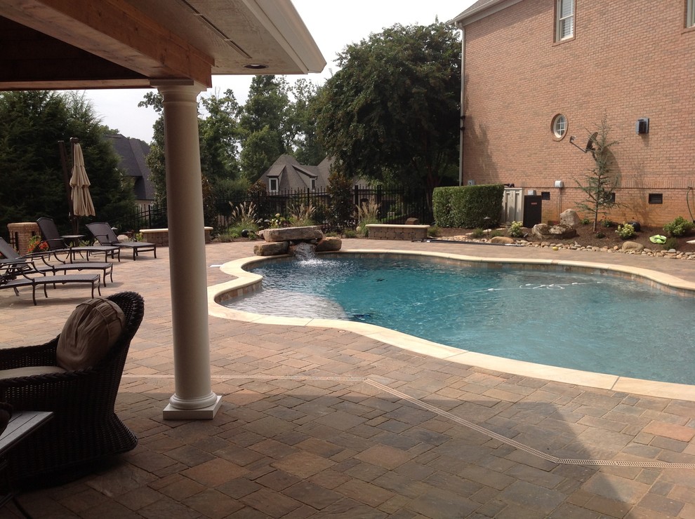 Photo of an expansive classic back custom shaped swimming pool in Other with a water feature and concrete paving.