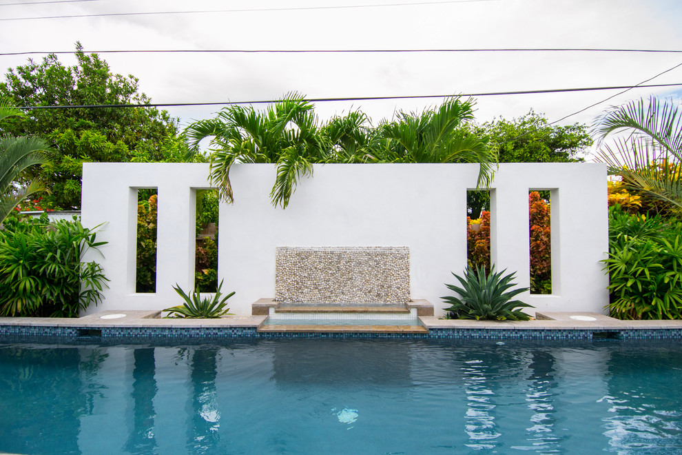 Modelo de piscina con fuente tropical de tamaño medio rectangular en patio trasero con entablado