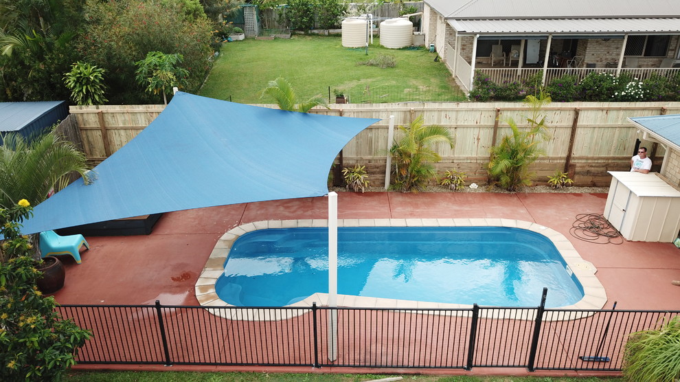 Ejemplo de piscina alargada tradicional de tamaño medio a medida en patio trasero con adoquines de hormigón