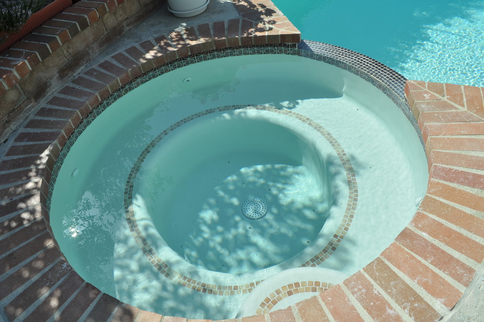 Modelo de piscinas y jacuzzis alargados tradicionales de tamaño medio tipo riñón en patio trasero con losas de hormigón