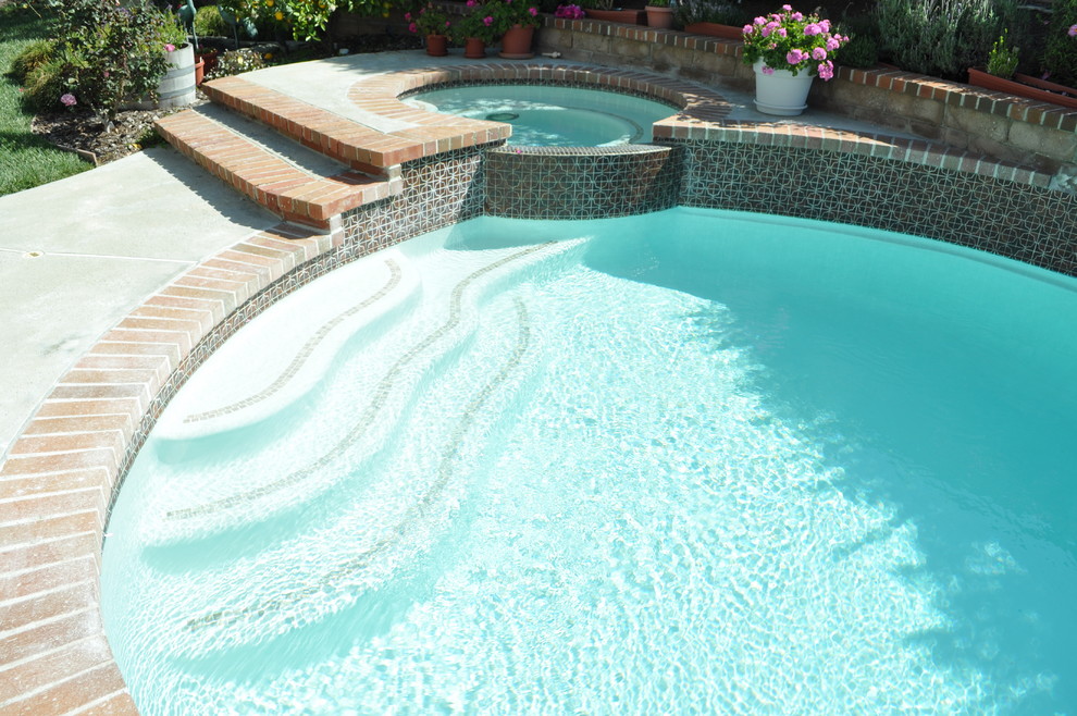Modelo de piscinas y jacuzzis alargados clásicos de tamaño medio tipo riñón en patio trasero con losas de hormigón