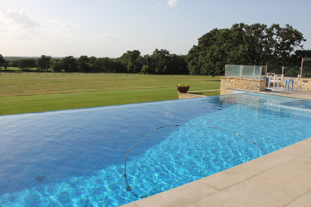 Immagine di una grande piscina a sfioro infinito country rettangolare dietro casa con una vasca idromassaggio e pavimentazioni in pietra naturale