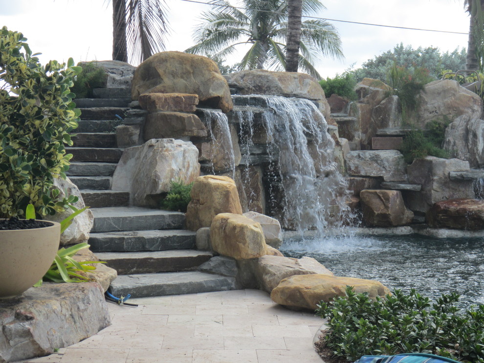 Diseño de piscina con fuente alargada tropical de tamaño medio a medida en patio trasero con adoquines de piedra natural