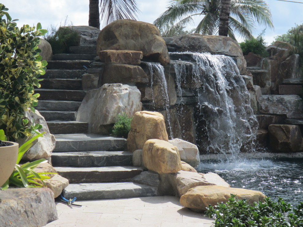 Mittelgroßes Sportbecken hinter dem Haus in individueller Form mit Wasserspiel und Natursteinplatten in Miami