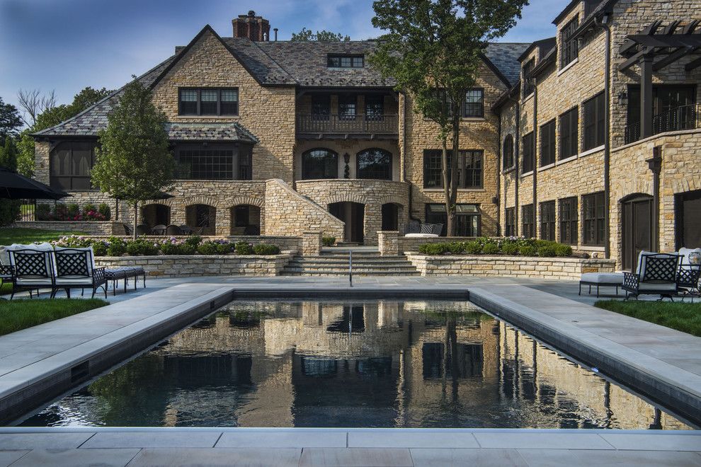 Modelo de piscina clásica de tamaño medio rectangular en patio trasero con adoquines de piedra natural