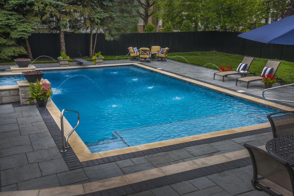 Immagine di una piscina classica rettangolare di medie dimensioni e dietro casa con fontane e pavimentazioni in pietra naturale