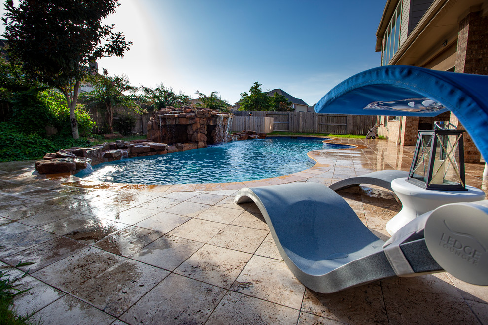 This is an example of a large world-inspired back custom shaped natural swimming pool in Houston with a water feature and natural stone paving.