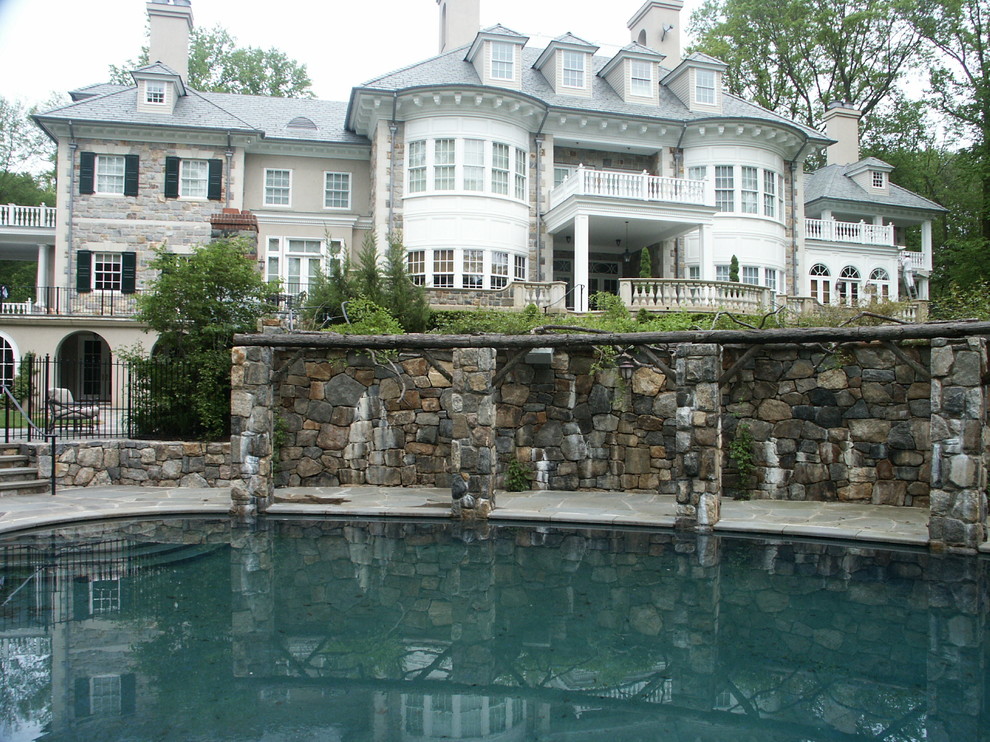 Esempio di un'ampia piscina monocorsia tradizionale rotonda dietro casa con pavimentazioni in pietra naturale