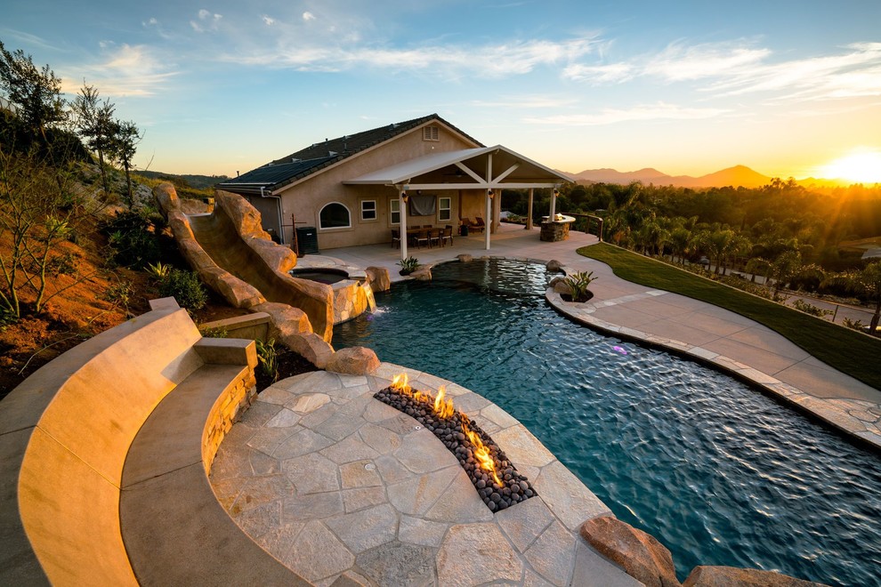 Imagen de piscina con tobogán alargada contemporánea grande a medida en patio trasero con adoquines de hormigón