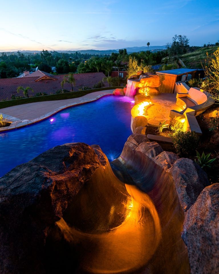 Imagen de piscina con tobogán alargada actual grande a medida en patio trasero con adoquines de hormigón