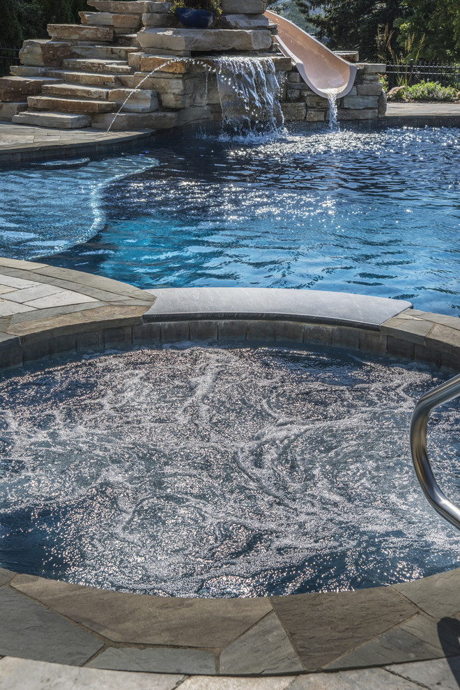 На фото: бассейн среднего размера, произвольной формы на заднем дворе в стиле рустика с водной горкой и покрытием из каменной брусчатки с