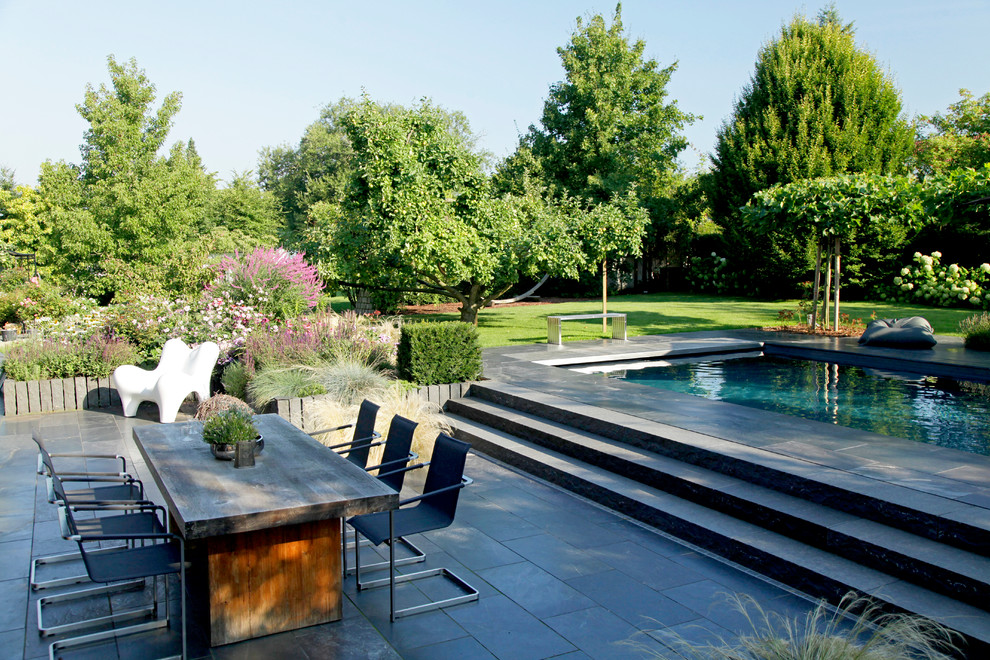 Foto de piscina alargada actual grande rectangular en patio trasero con adoquines de piedra natural