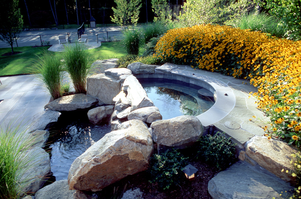 Modelo de piscinas y jacuzzis naturales clásicos redondeados en patio trasero con adoquines de piedra natural