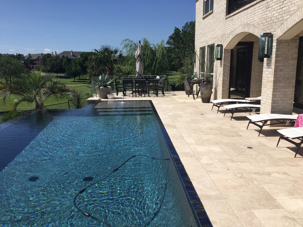Ejemplo de piscina con fuente infinita clásica grande rectangular en patio trasero con adoquines de piedra natural