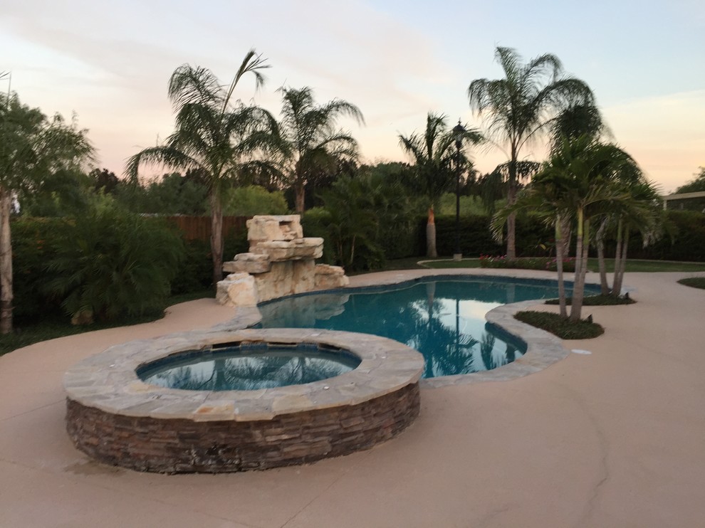 Imagen de piscina con fuente natural tropical de tamaño medio a medida en patio trasero con adoquines de piedra natural