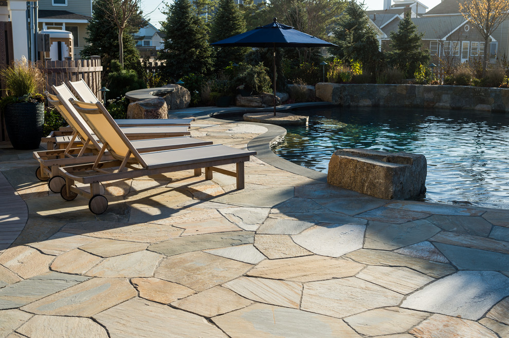This is an example of a medium sized rustic back custom shaped natural swimming pool in New York with a water feature and natural stone paving.