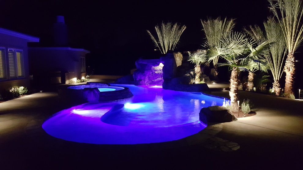 Immagine di una grande piscina monocorsia tropicale a "C" dietro casa con pavimentazioni in pietra naturale e una vasca idromassaggio