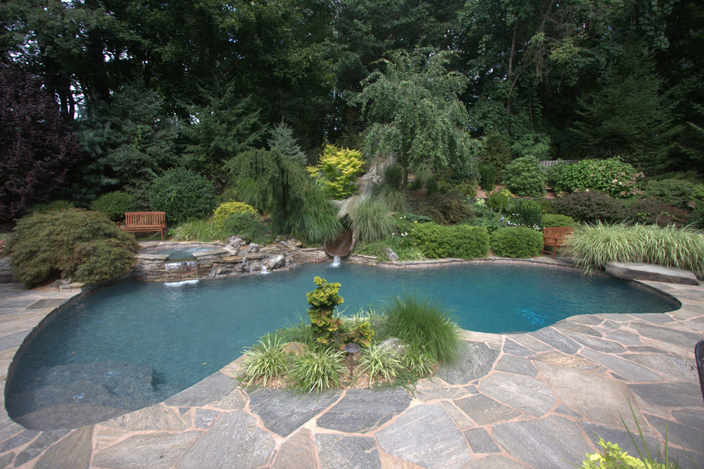 This is an example of a large rustic back custom shaped swimming pool in New York with a water slide and stamped concrete.