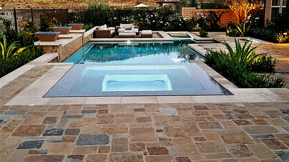 Cette image montre un grand couloir de nage arrière design rectangle avec un bain bouillonnant et des pavés en pierre naturelle.