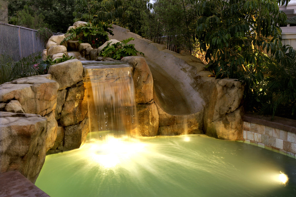 Medium sized world-inspired back custom shaped swimming pool in Orange County with a water slide and concrete slabs.