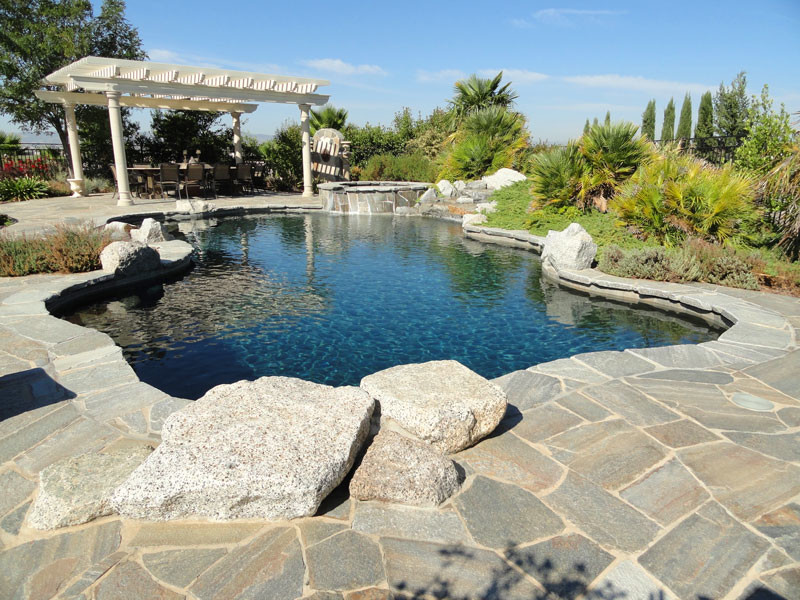 Esempio di una grande piscina naturale design personalizzata dietro casa con una vasca idromassaggio e pavimentazioni in pietra naturale