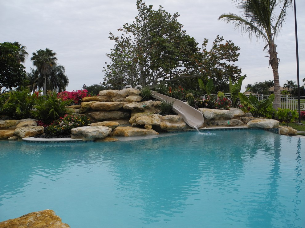 Cette photo montre une grande piscine à débordement et arrière exotique rectangle avec des pavés en pierre naturelle et un toboggan.