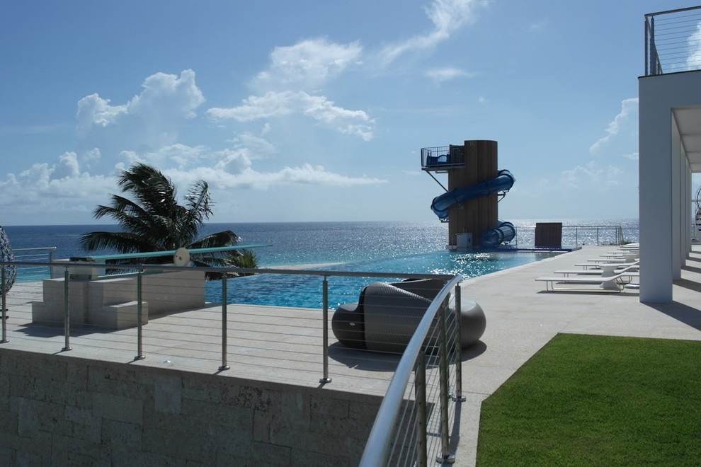 Immagine di una piscina a sfioro infinito tropicale personalizzata di medie dimensioni e dietro casa con un acquascivolo e lastre di cemento