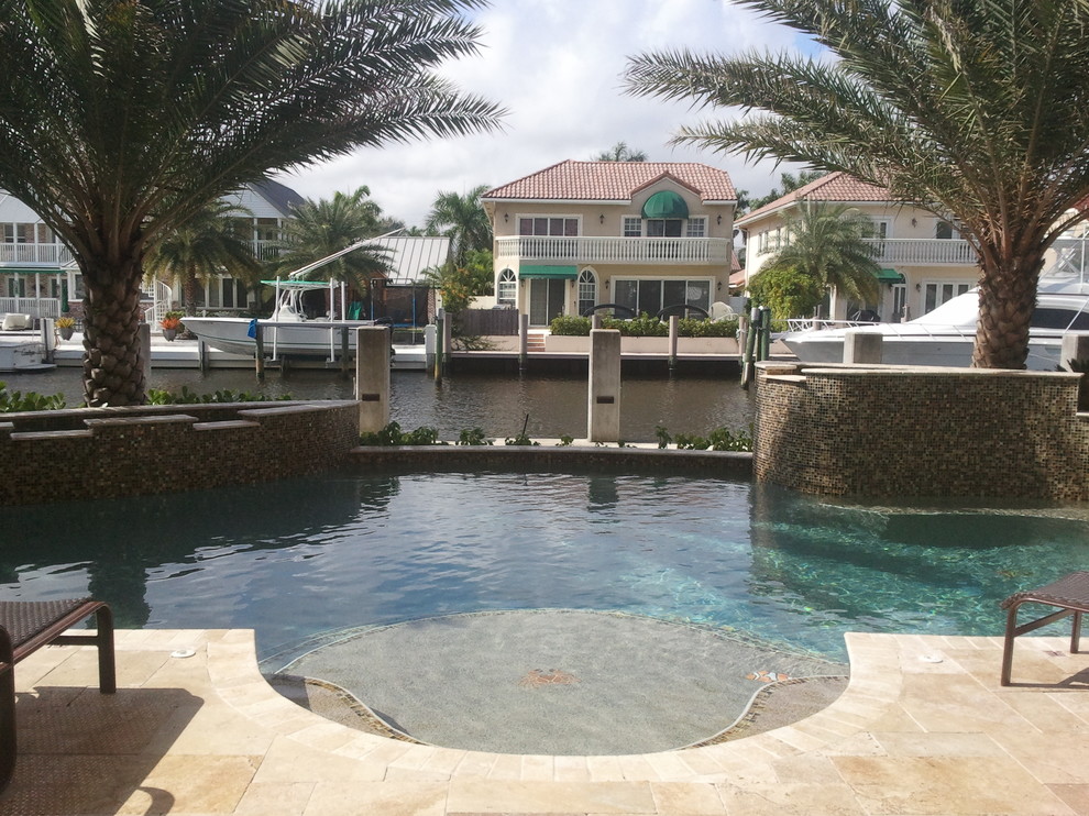This is an example of a medium sized contemporary back custom shaped swimming pool in Miami with a water feature and natural stone paving.