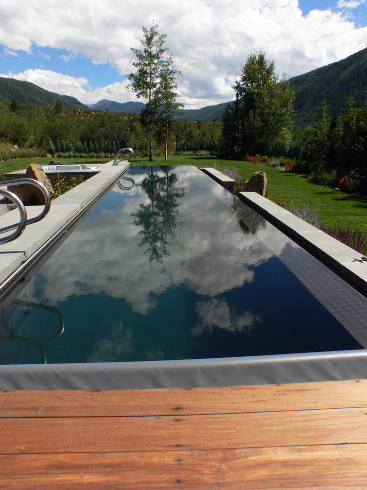 Imagen de piscina infinita moderna grande a medida en patio trasero con adoquines de piedra natural