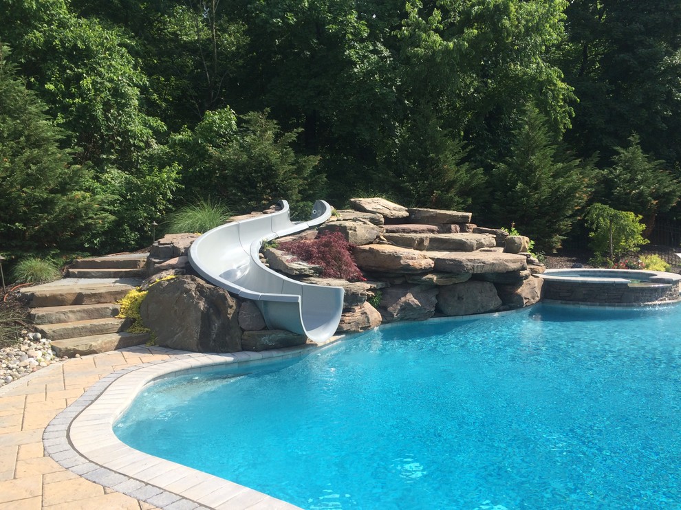 Modelo de piscina con tobogán tradicional grande a medida en patio trasero con adoquines de hormigón