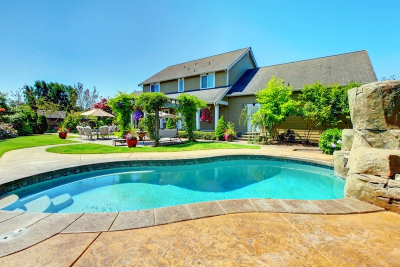 Diseño de piscina alargada clásica grande tipo riñón en patio trasero con losas de hormigón