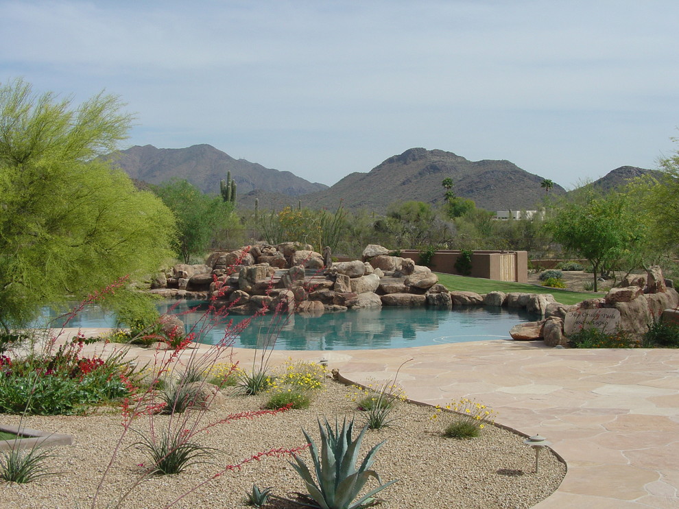 Design ideas for an expansive mediterranean back custom shaped natural swimming pool in Phoenix with a water feature and natural stone paving.
