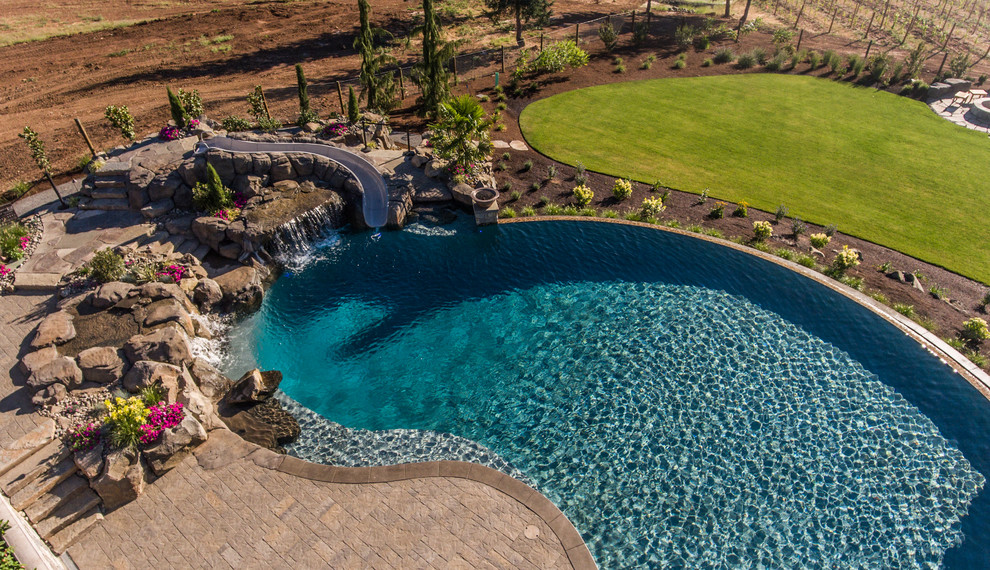 Ispirazione per un'ampia piscina a sfioro infinito mediterranea personalizzata dietro casa con un acquascivolo e pavimentazioni in cemento