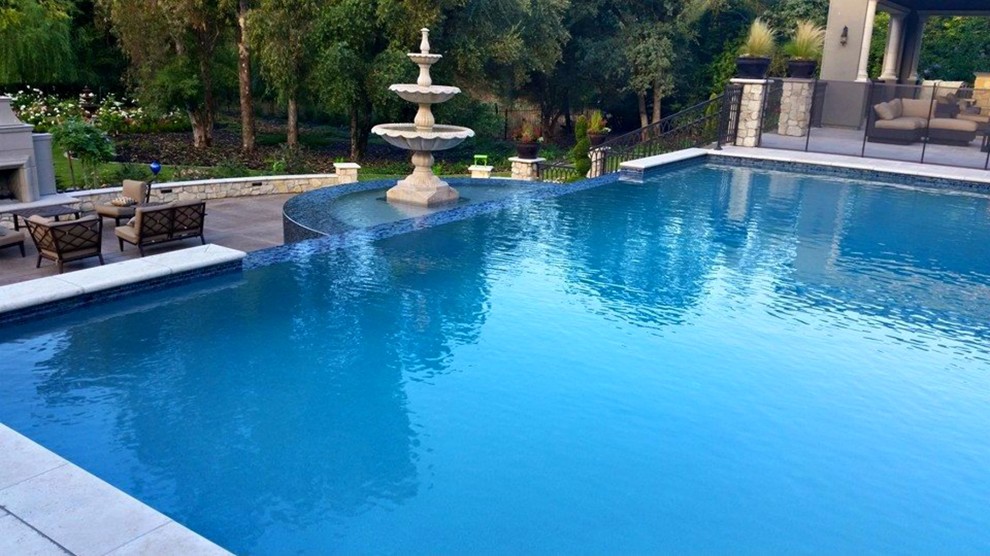 Modelo de piscina con fuente infinita mediterránea grande rectangular en patio trasero con losas de hormigón