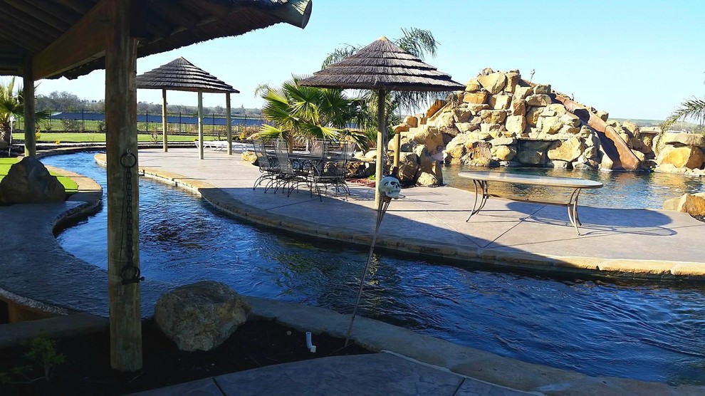 Imagen de piscina con tobogán natural tropical extra grande a medida en patio trasero con adoquines de hormigón